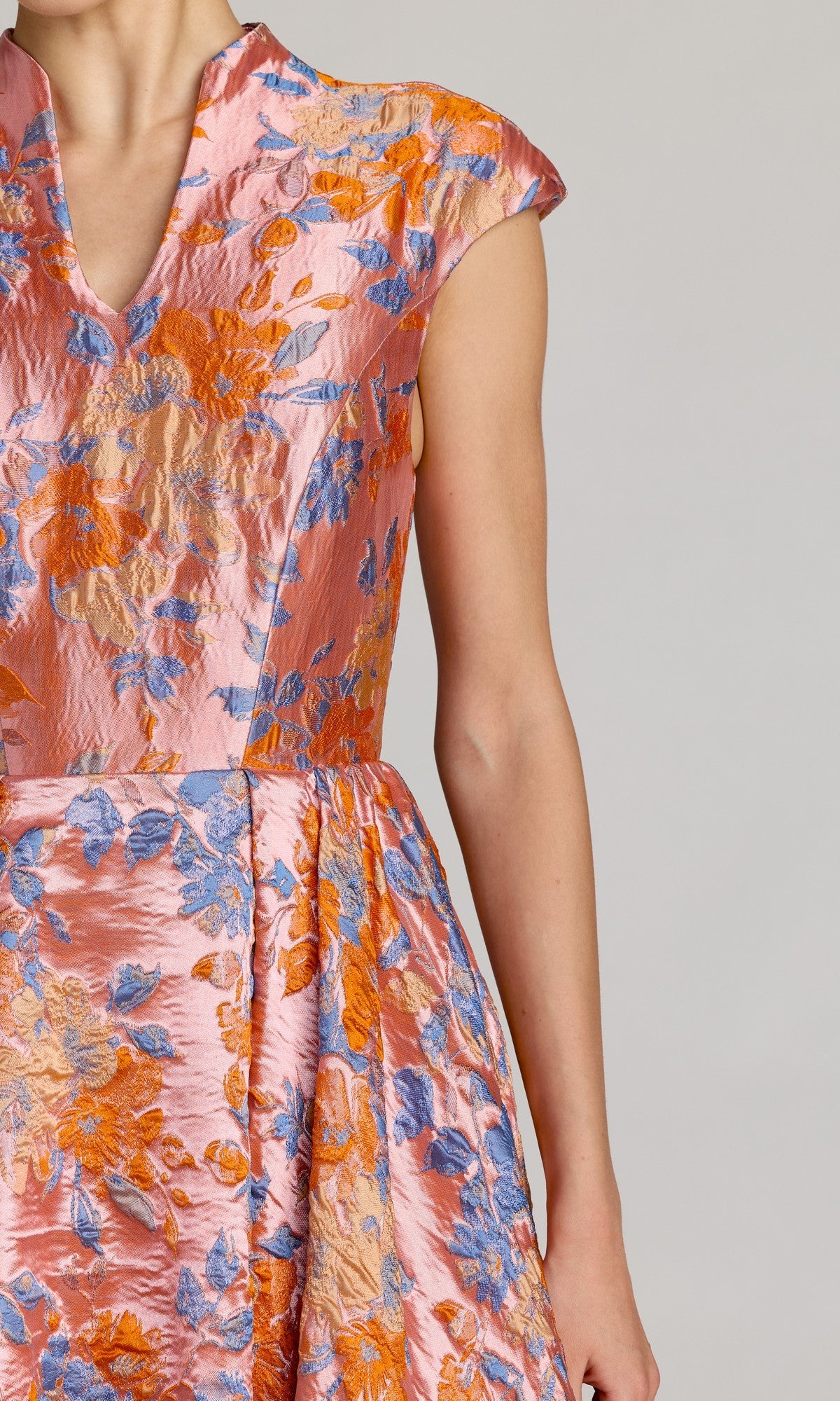 A woman models the Mac Duggal 69171 Long Formal Dress, a pink, orange, and blue floral brocade gown with cap sleeves and a V-neck, shown from shoulders to mid-thigh against a plain background.